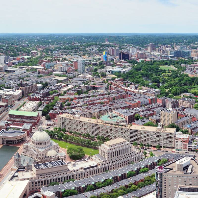 Panoramic aerial view of a large cityscape with residential and commercial buildings, green parks, and winding roads.