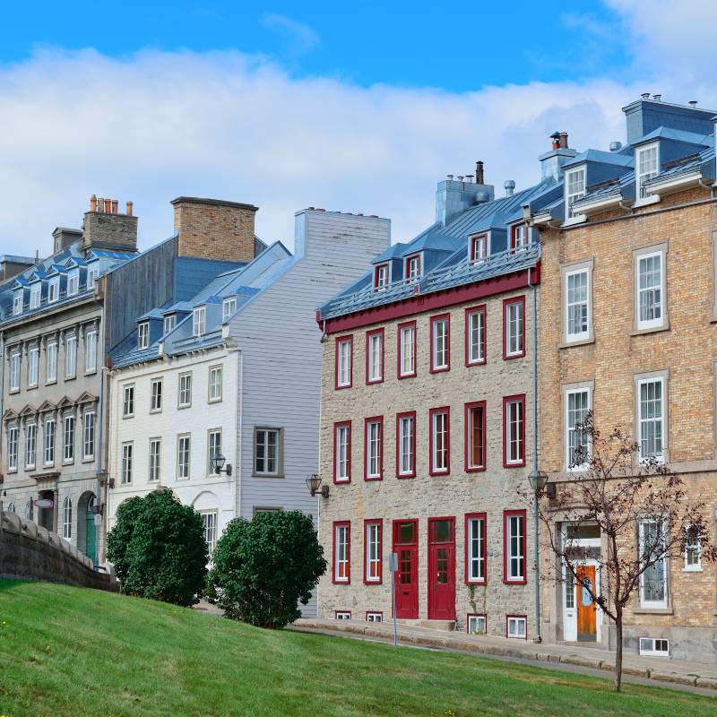 View of a traditional European-style townhouses with blue rooftops and large windows situated along a grassy slope.
